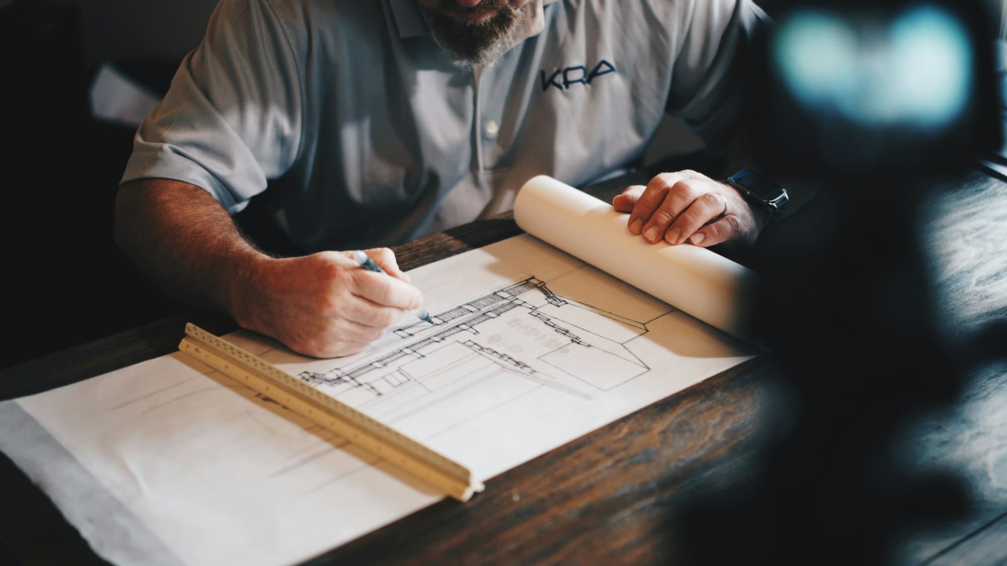 Hands working over technical drawings with a scale rule and pencil.