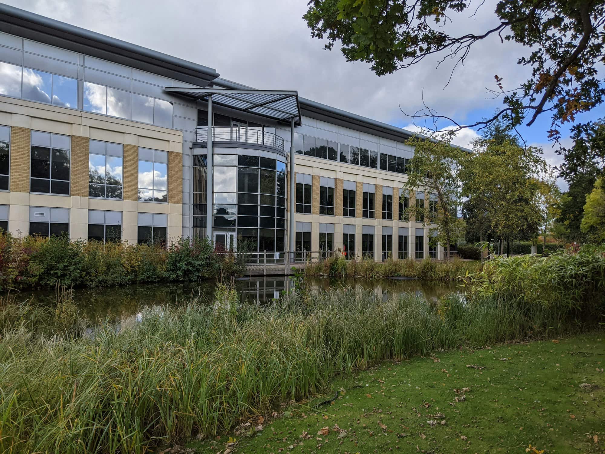 A low-rise modern office building beside water on a landscaped business park.