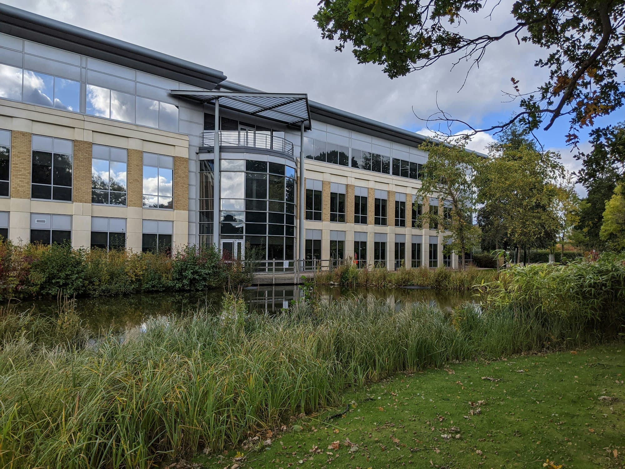 A low-rise modern office building beside water on a landscaped business park.